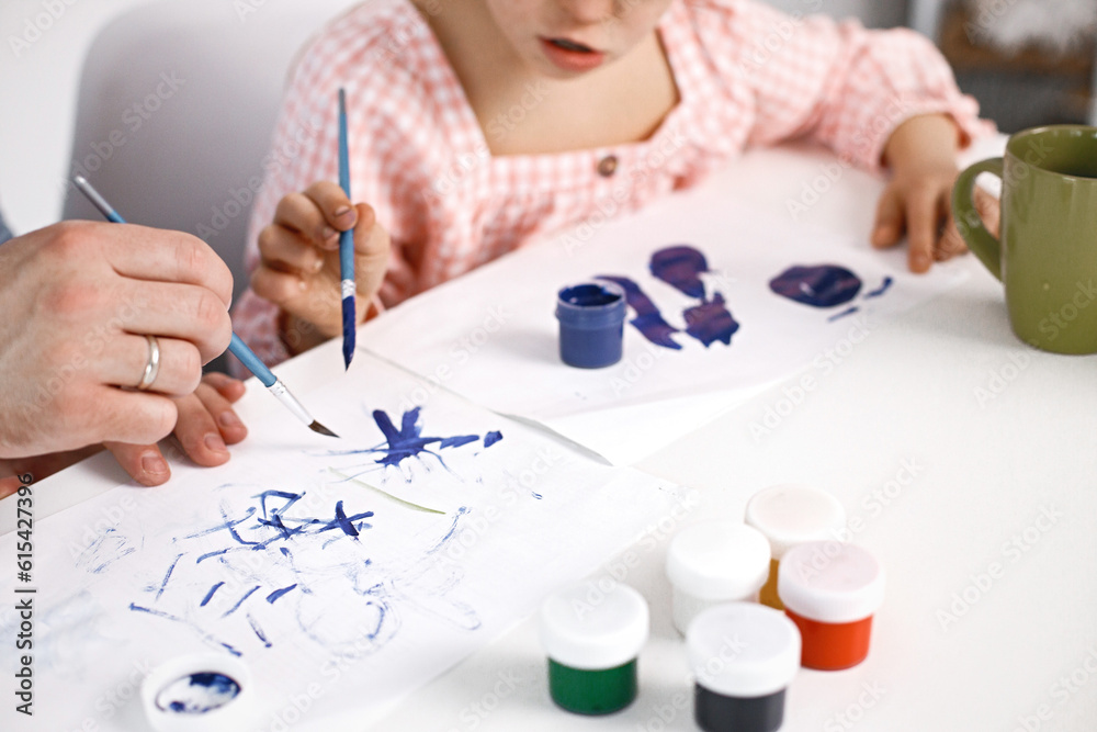 Cropped photo of girl with Down syndrome drawing on a paper with blue paints