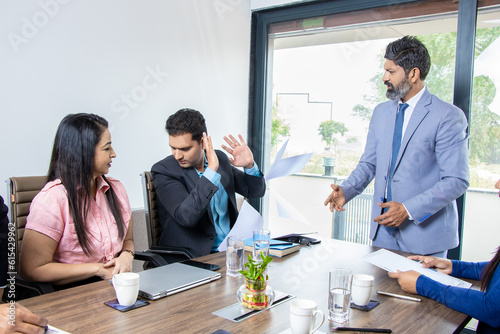 Angry indian boss screaming at male employee for bad work, Businessman ceo scolding incompetent manager blaming and throwing papers at his face for mistake in financial report conference meeting. photo