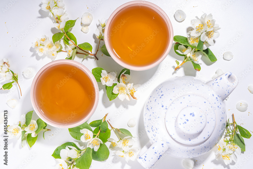 Organic herbal health drink. Jasmine flowers green tea, in white mugs, with teapot, on white table, with blooming jasmine flowers Organic herbal health drink. Jasmine flowers green tea, in white mugs, with teapot, on white table, with blooming jasmine flowers