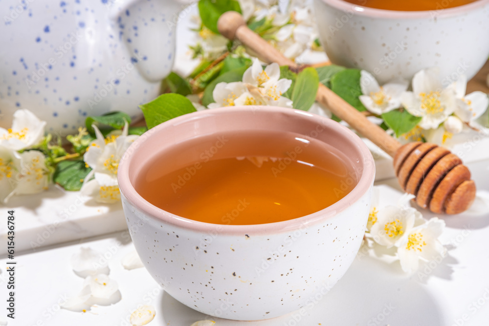 Organic herbal health drink. Jasmine flowers green tea, in white mugs, with teapot, on white table, with blooming jasmine flowers Organic herbal health drink. Jasmine flowers green tea, in white mugs, with teapot, on white table, with blooming jasmine flowers