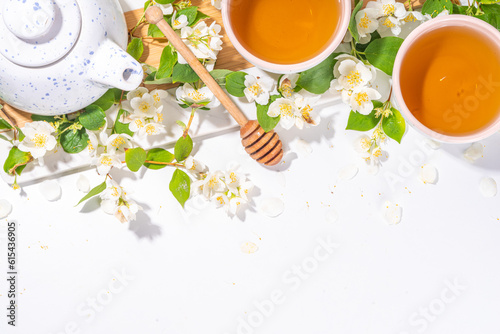 Organic herbal health drink. Jasmine flowers green tea, in white mugs, with teapot, on white table, with blooming jasmine flowers 