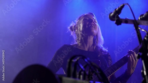 Caucasian vocalist singing energetically with microphone on stage while playing guitar in slow motion