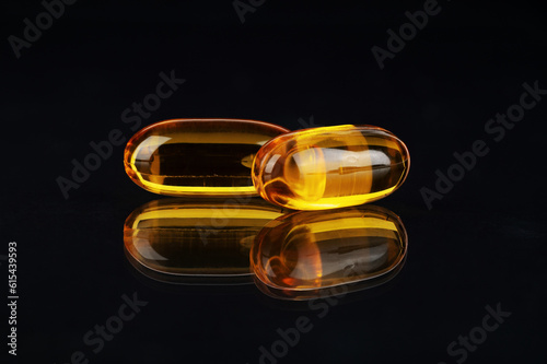 Cod liver oil omega 3 gel capsules on black background with reflection.