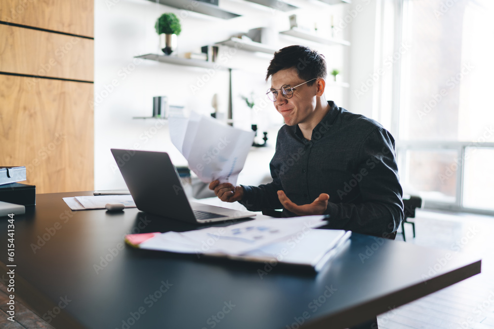 Smiling young man sitting with papers and laptop at table Smiling young man sitting with papers and laptop at table