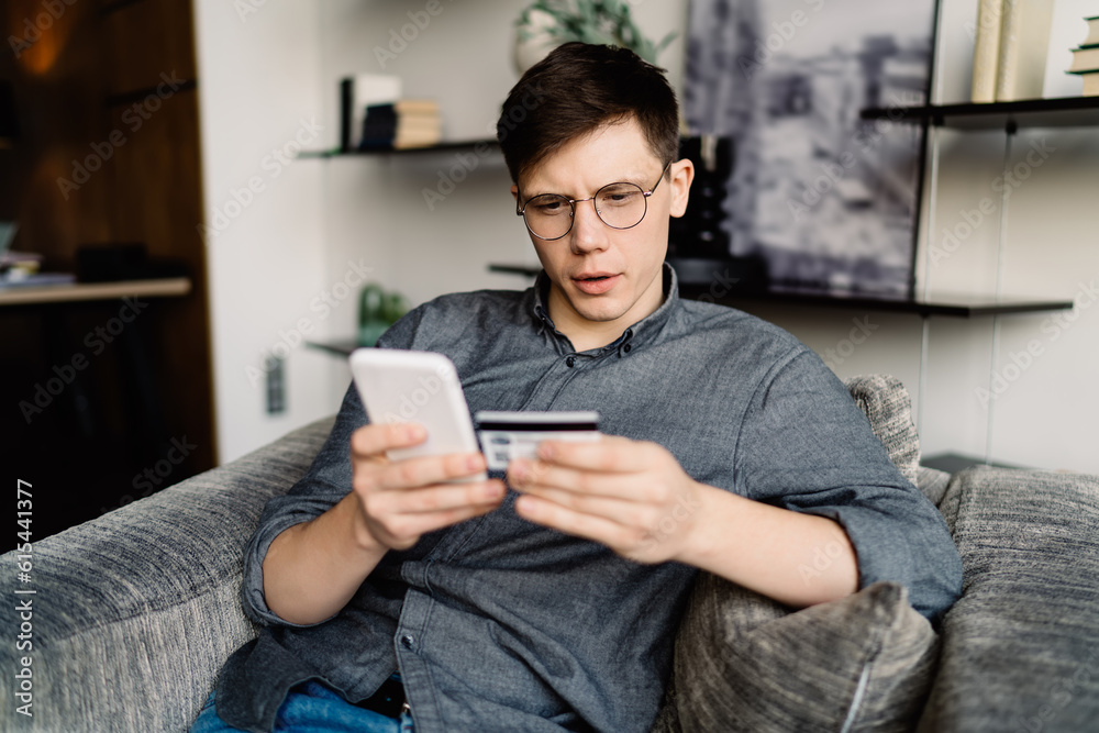 Focused man using smartphone and credit card for online payment