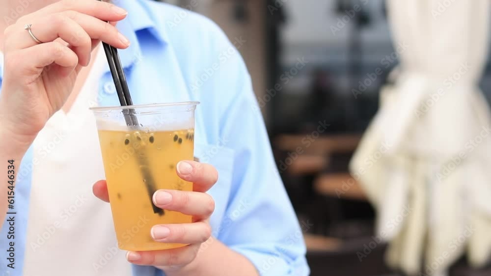 Passion fruit lemonade. Summer drink in the hands of a girl. Takeaway lemonade. Cold lemonade with ice in a female hand against a summer street cafe Passion fruit lemonade. Summer drink in the hands of a girl. Takeaway lemonade. Cold lemonade with ice in a female hand against a summer street cafe