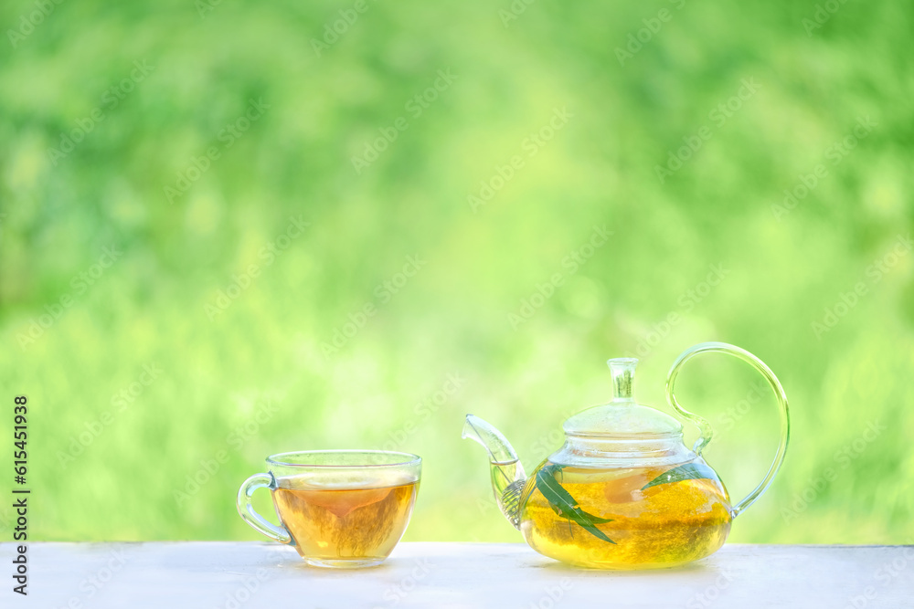 glass teapot and cup with herbal tea close up on table in garden, natural abstract green background. summer season. relax time. freshness calming useful tea. Tea party. template for design. copy space glass teapot and cup with herbal tea close up on table in garden, natural abstract green background. summer season. relax time. freshness calming useful tea. Tea party. template for design. copy space