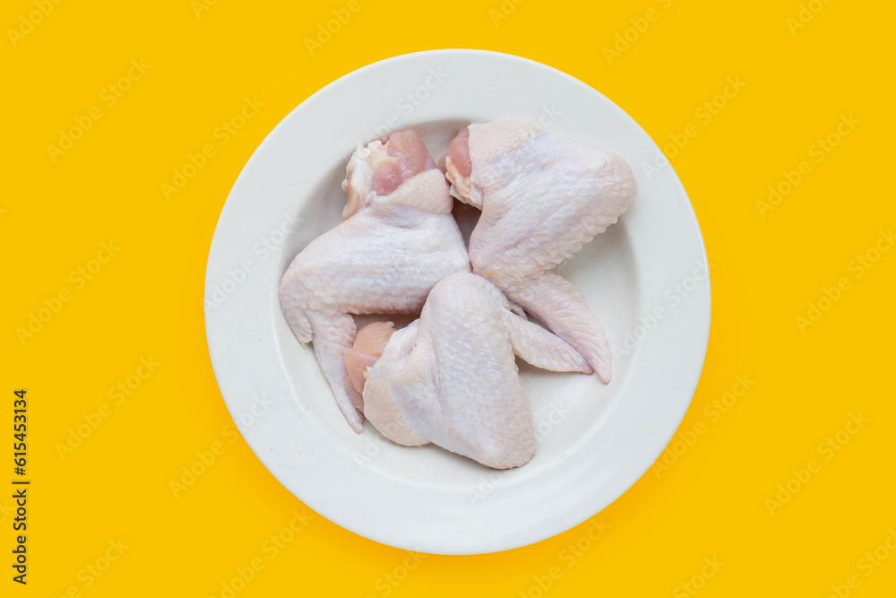Fresh raw chicken wings in white plate on yellow background. Fresh raw chicken wings in white plate on yellow background.