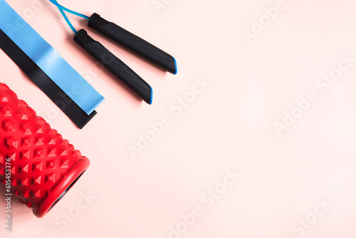 Set of sports equipment on a light pink background. Foam roller, resistance bands, jump rope. Home fitness workout concept. Healthy lifestyle idea. Flat lay top view copy space.
