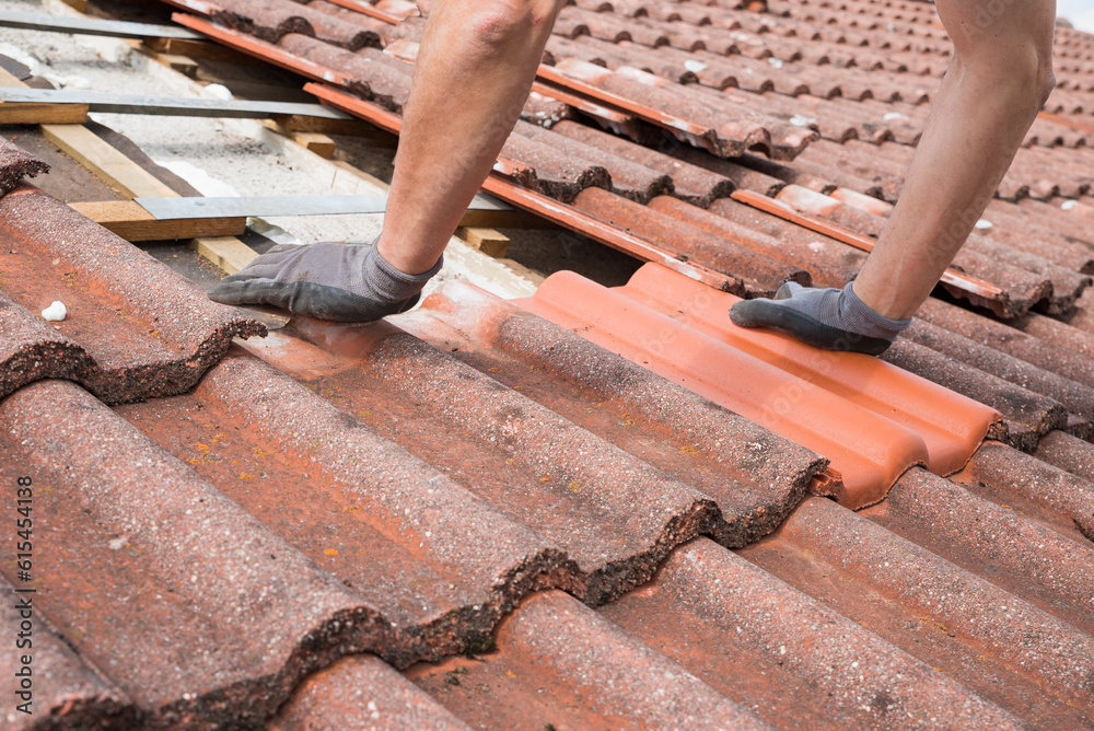 man replaces broken roof shingles on the rooftop with new ones - obrazy, fototapety, plakaty 