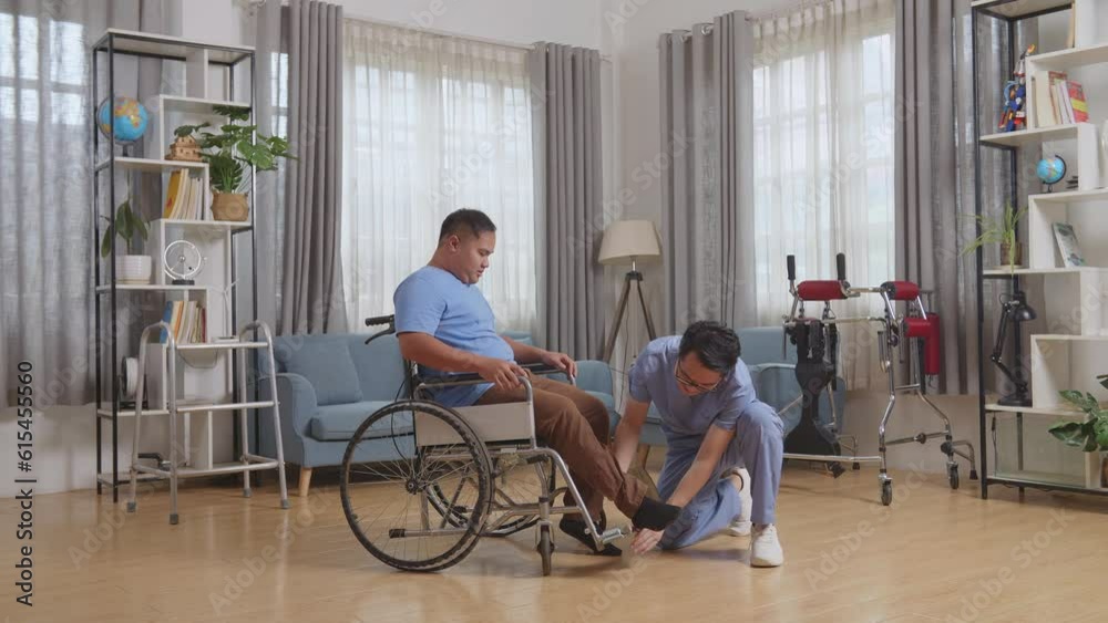 Full Body Side View Of Asian Male Nurse Helping A Patient In Wheelchair Putting Feet On Footrest After A Physical Therapy At Home
