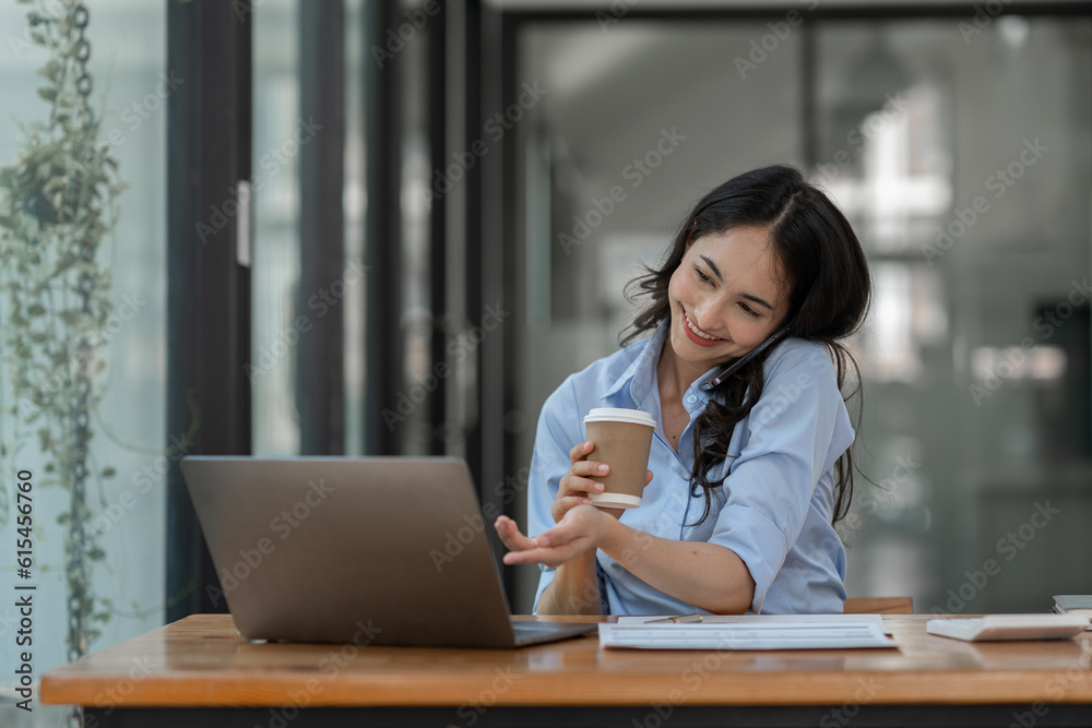 Asian businesswoman holding cup of coffee and financial business papers sitting resting while working using laptop, calculator to analyze investment finance report, startup business concept. Asian businesswoman holding cup of coffee and financial business papers sitting resting while working using laptop, calculator to analyze investment finance report, startup business concept.