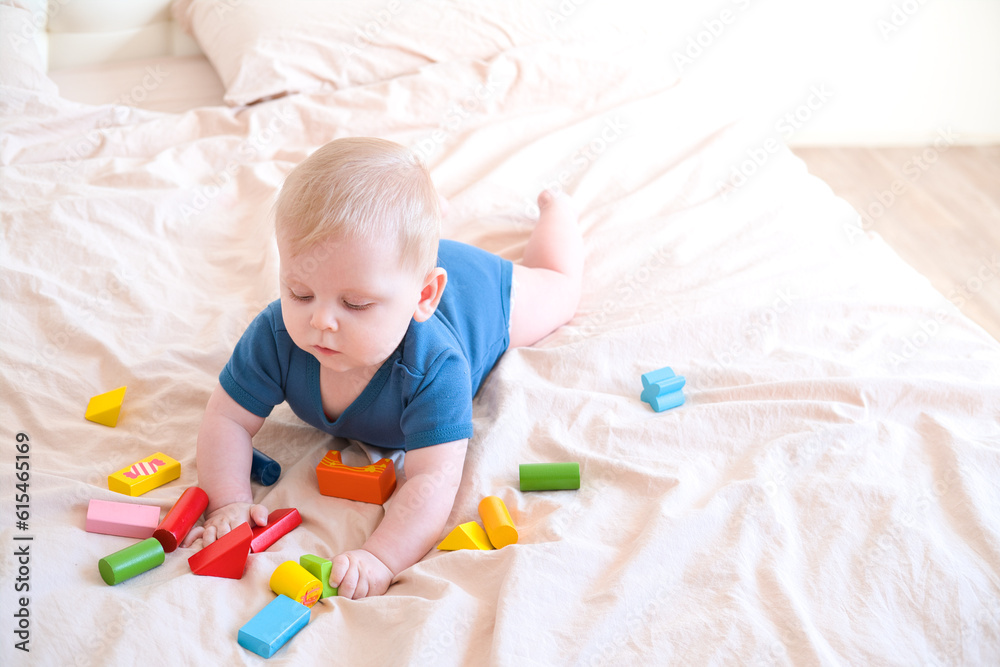 baby boy in blue bodysuit playing with colorful wooden eco toys on bed baby boy in blue bodysuit playing with colorful wooden eco toys on bed