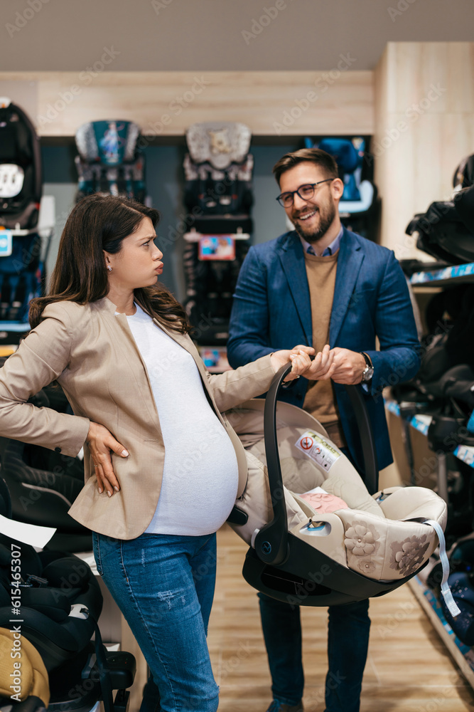 Attractive middle age couple enjoying in buying baby stroller and car seat. Heterosexual couple in baby shop or store. Child expecting concept.
