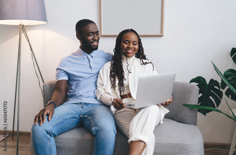 Black couple sitting on sofa using netbook at home