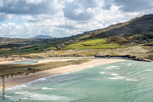 Scenic view of the turquoise waves of the Atlantic lapping the sandy shore of the beach at Barleycove with the hills and farmland of the countryside in the background; Barleycove, West Cork, Ireland photo