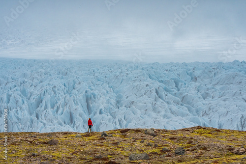 Woman walking on the tundra in front of an impressive glacier with its jagged blue ice and foggy atmosphere along the South Coast of Iceland; South Iceland, Iceland