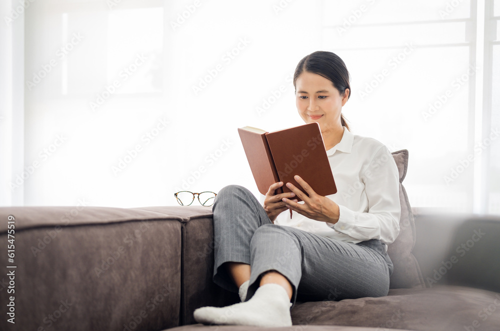 Senior asian woman Reading Book Sitting On Couch At Home. Retired female Enjoying Reading New Novel Or Business Literature On Weekend. Retirement Leisure Concept Senior asian woman Reading Book Sitting On Couch At Home. Retired female Enjoying Reading New Novel Or Business Literature On Weekend. Retirement Leisure Concept