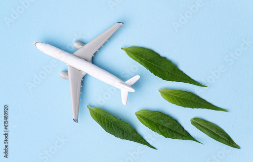 Sustainable Aviation Fuel. White airplane model, fresh green leaves on blue background.