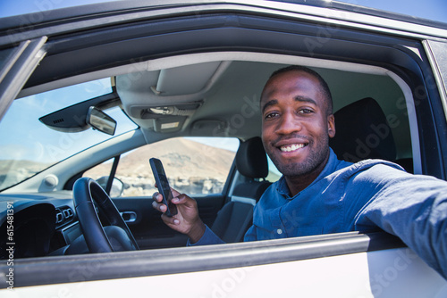 A smiling businessman sitting in his car takes a selfie while using his smartphone