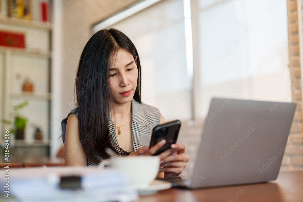 Close-up, pretty Asian woman sits on mobile phone with smiling face talk boyfriend through chat application on mobile phone, there is laptop computer on table, It's computer that women use work. Close-up, pretty Asian woman sits on mobile phone with smiling face talk boyfriend through chat application on mobile phone, there is laptop computer on table, It's computer that women use work.
