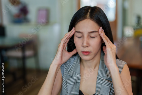 Close-up of beautiful Asian woman's face is massaging her head with both hands. Having headaches due to work stress that cannot verify the authenticity of the shop account to relax