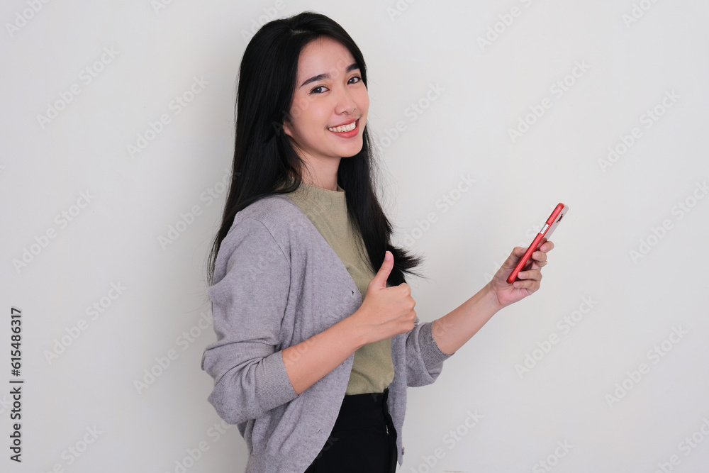 Naklejka premium Side view of young woman smiling and give thumb up while holding a mobile phone