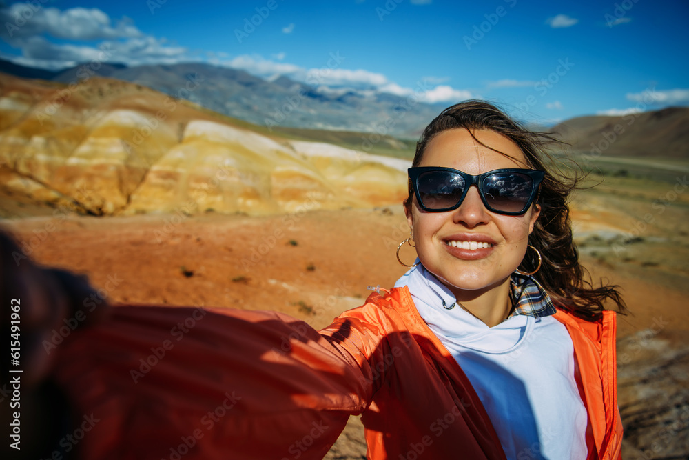 Happy young woman takes a selfie with amazing mountain view. Excited brunette enjoying vacation. Female traveller portrait.