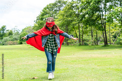 Caucasian girl having fun wearing red mask, red cape, running cross like a fly in the park. The superhero concept saves the global environment and enjoylite.