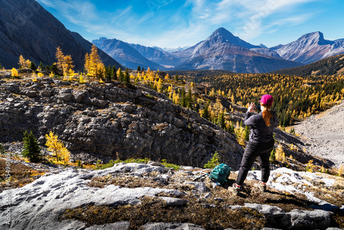 A woman in nature taking a photograph of mountain larch trees in Autumn colours overlooking the Canadian Rocky Mountains in Kananaskis near Banff Canada. photo