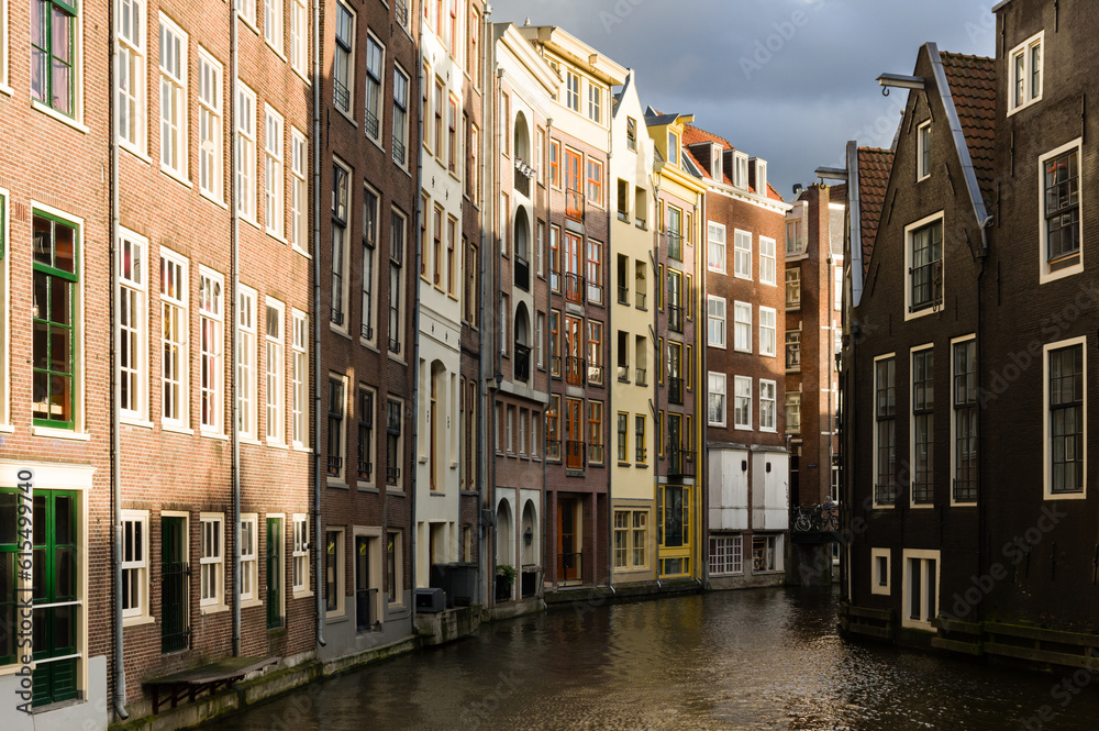 Sunlit facades of houses in Amsterdam separated by a canal