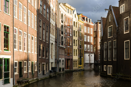 Sunlit facades of houses in Amsterdam separated by a canal