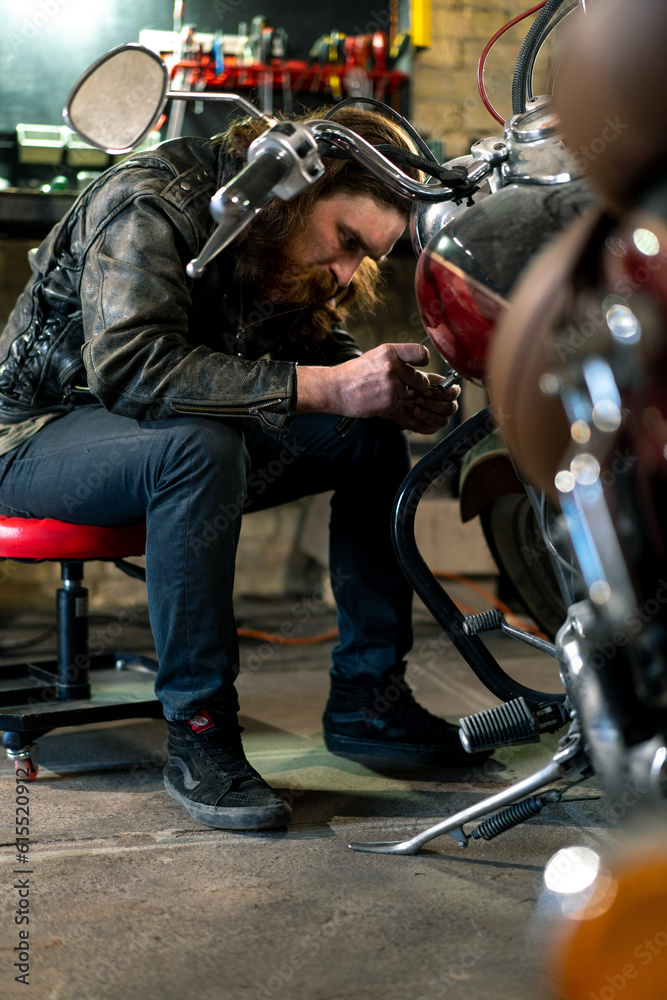 Obraz premium Creative authentic motorcycle workshop Garage redhead bearded biker mechanic is concentrating on repairing motorcycle