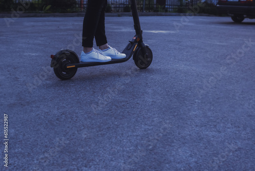 Girl in white sneakers driving an electric scooter in dusk