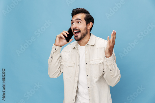 Portrait of a brunette man talking on the phone mobile and internet online, smile with teeth surprise and happiness, on a blue background in a white T-shirt, copy space 