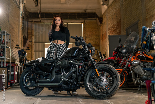 Creative authentic motorcycle workshop garage beautiful young biker girl standing near a cool motorcycle