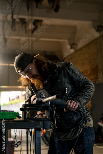 Creative authentic motorcycle workshop redhead bearded brutal biker works with circular saw Sparks fly from hot metal