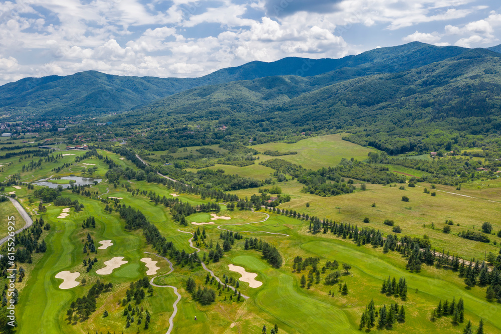 Landscape with golf course near the mountain and lakeside in aerial view.