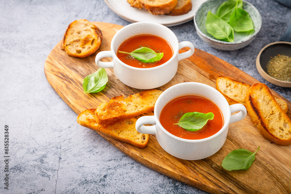 Homemade tomato soup with basil, toast and olive oil on a wooden cutting board. Homemade tomato soup with basil, toast and olive oil on a wooden cutting board.