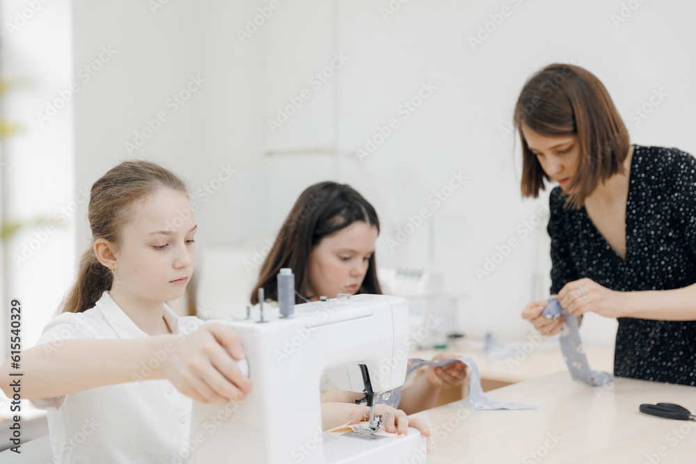 Education work in school for two girl child. Smiling female seamstress talking with children. Dressmaker conducts sewing masterclass Education work in school for two girl child. Smiling female seamstress talking with children. Dressmaker conducts sewing masterclass