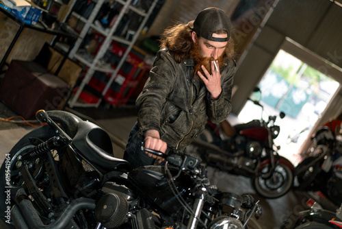 Creative authentic motorcycle workshop Garage redhead bearded biker mechanic smoking cigarette near motorcycle © Guys Who Shoot