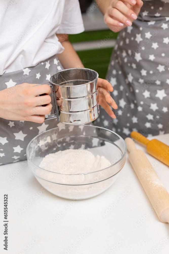 The process of sifting flour and making baking dough. A teenager's hands hold a metal cup with flour. The flour is falling. The process of sifting flour and making baking dough. A teenager's hands hold a metal cup with flour. The flour is falling.