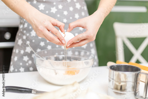 A woman's hands crack an egg into a bowl of flour at home. The process of making cookie dough.