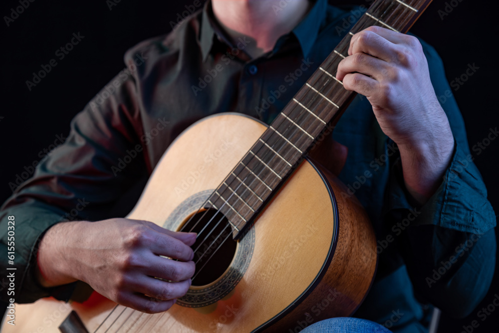 Fototapeta premium The guy in the dark shirt is plucking the strings of a six-string guitar