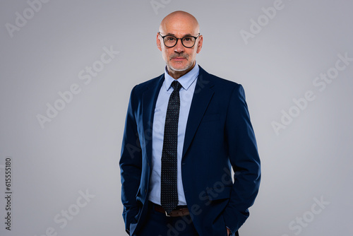 Foto Portrait of handsome mature businessman wearing suit and standing at grey backgr