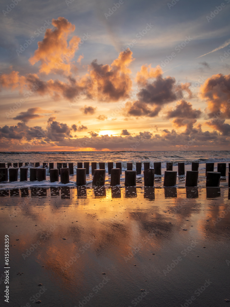 Obraz premium Sunset with colorful sky and clouds and wooden posts at Westenschouwen, Zeeland, the Netherlands