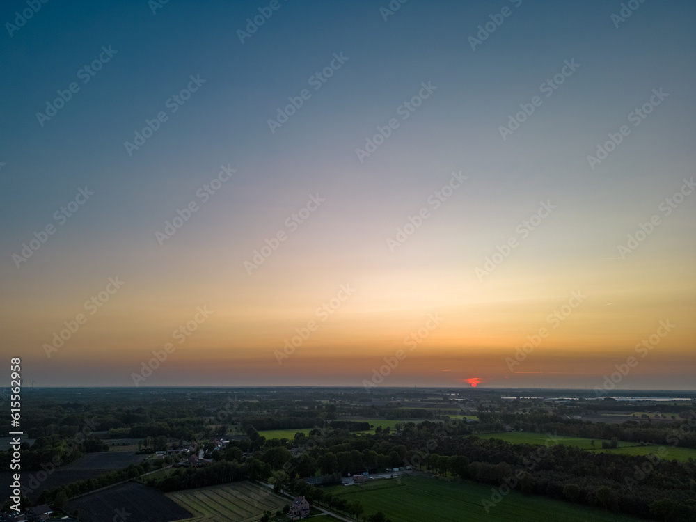 Aerial view of endless lush pastures and farmlands of Belgium under a colorful and dramatic sunset sky. Beautiful Irish countryside with emerald green fields and meadows. Rural landscape on sunset