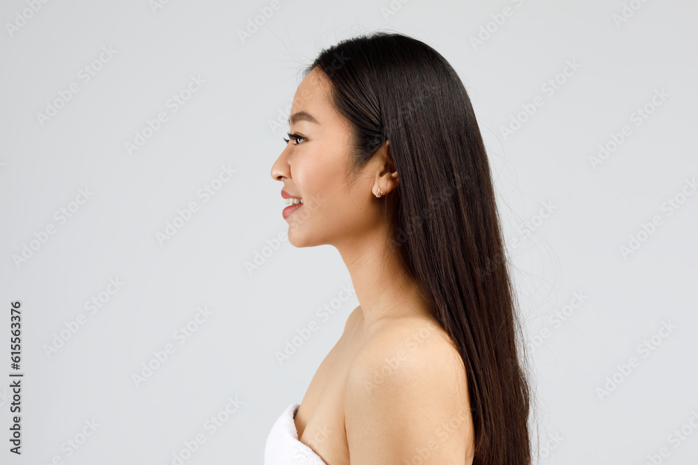 Profile portrait of happy beautiful asian woman with perfect skin and thick hair smiling, posing on grey background Profile portrait of happy beautiful asian woman with perfect skin and thick hair smiling, posing on grey background