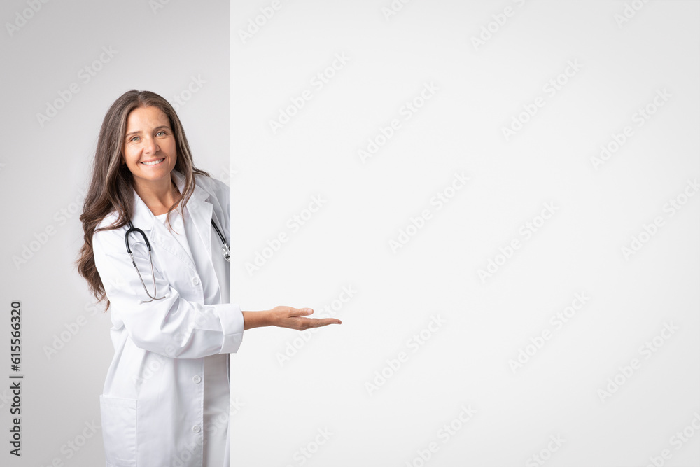 Medicine service advice. Smiling senior woman doctor in white coat pointing hand to big banner with empty space, banner Medicine service advice. Smiling senior woman doctor in white coat pointing hand to big banner with empty space, banner