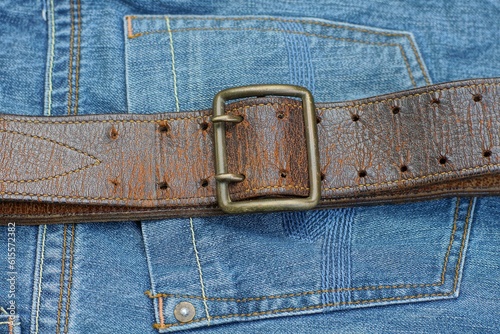 old army durable retro brown leather with a heavy golden iron buckle made in the USSR the belt lies on the blue pocket of denim pants